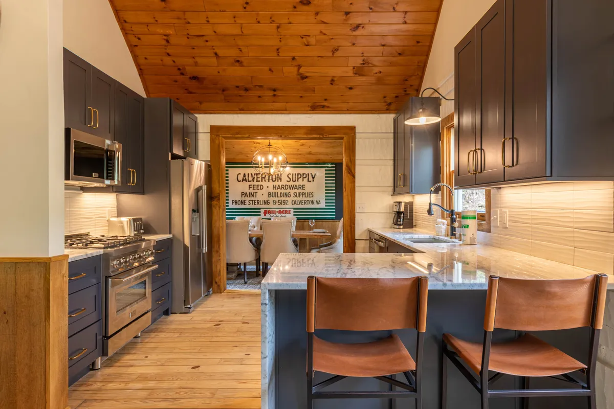 A chef-inspired kitchen and dining area with a prominent kitchen island, modern stainless appliances, and an open layout. The wooden ceiling and dining area create a seamless flow between cooking, dining, and socializing spaces. The scene is cozy and inviting, emphasizing ease and functionality.