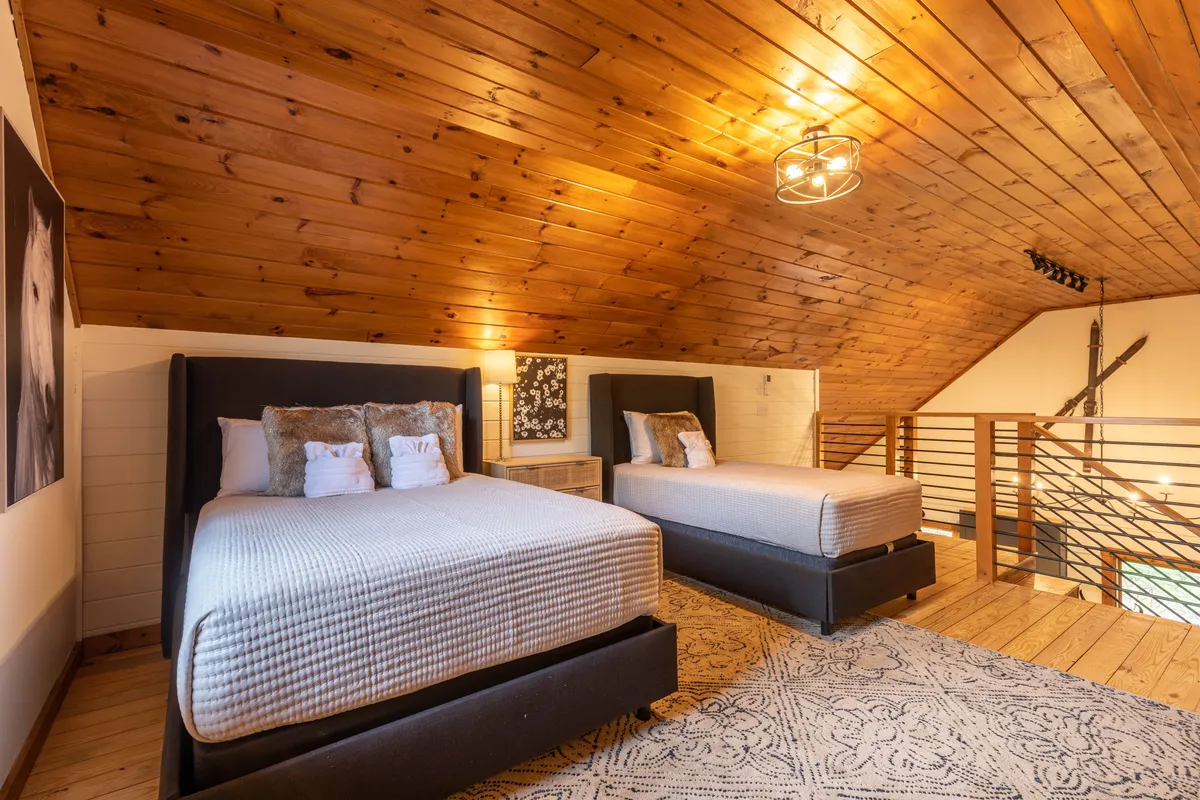 A spacious bedroom featuring two beds with plush headboards, warm wooden ceilings, a decorative rug, and large wall art of a horse. The inviting layout suggests flexibility for families or friends, with a cozy and welcoming ambiance.