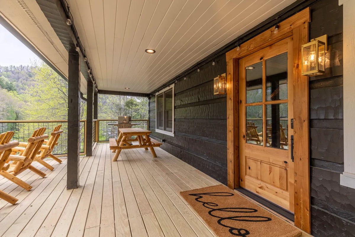 This image features a welcoming outdoor area with a wooden door, picnic table, and Adirondack chairs. The setup suggests a perfect spot for socializing, alfresco dining, and enjoying the natural surroundings, with direct access to the deck and seamless indoor-outdoor flow.