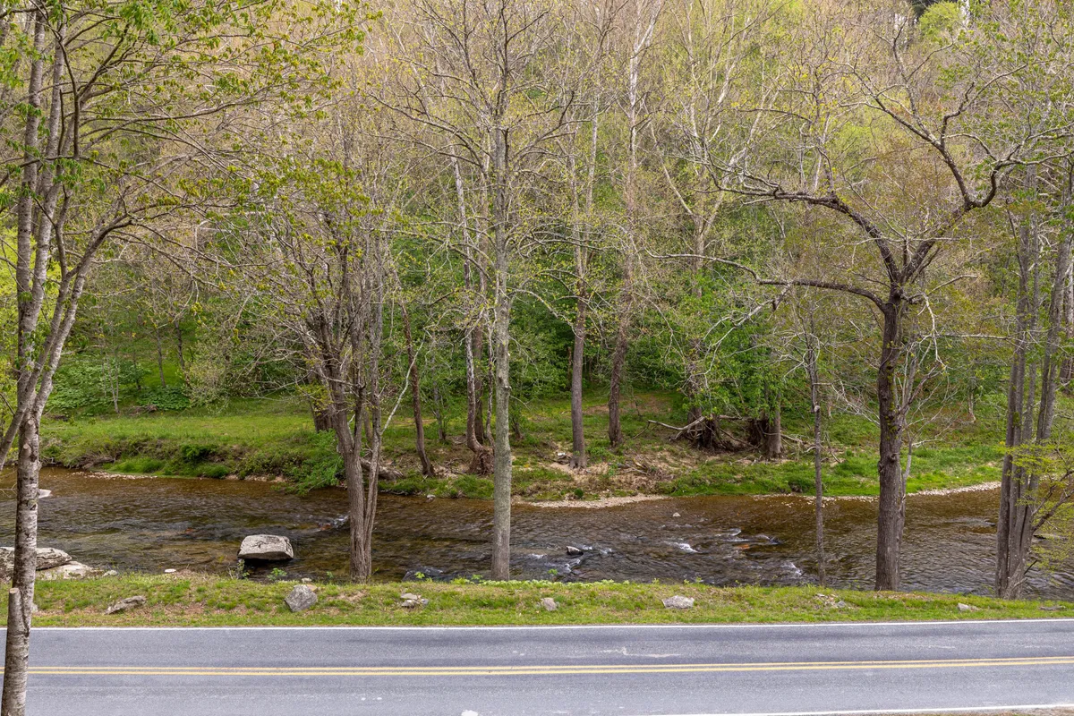 A sweeping view of the river, flanked by trees and a nearby road, suggesting easy access for walks, fishing, or picnicking. The landscape is open and inviting, with soft light capturing the calm mood of the area.