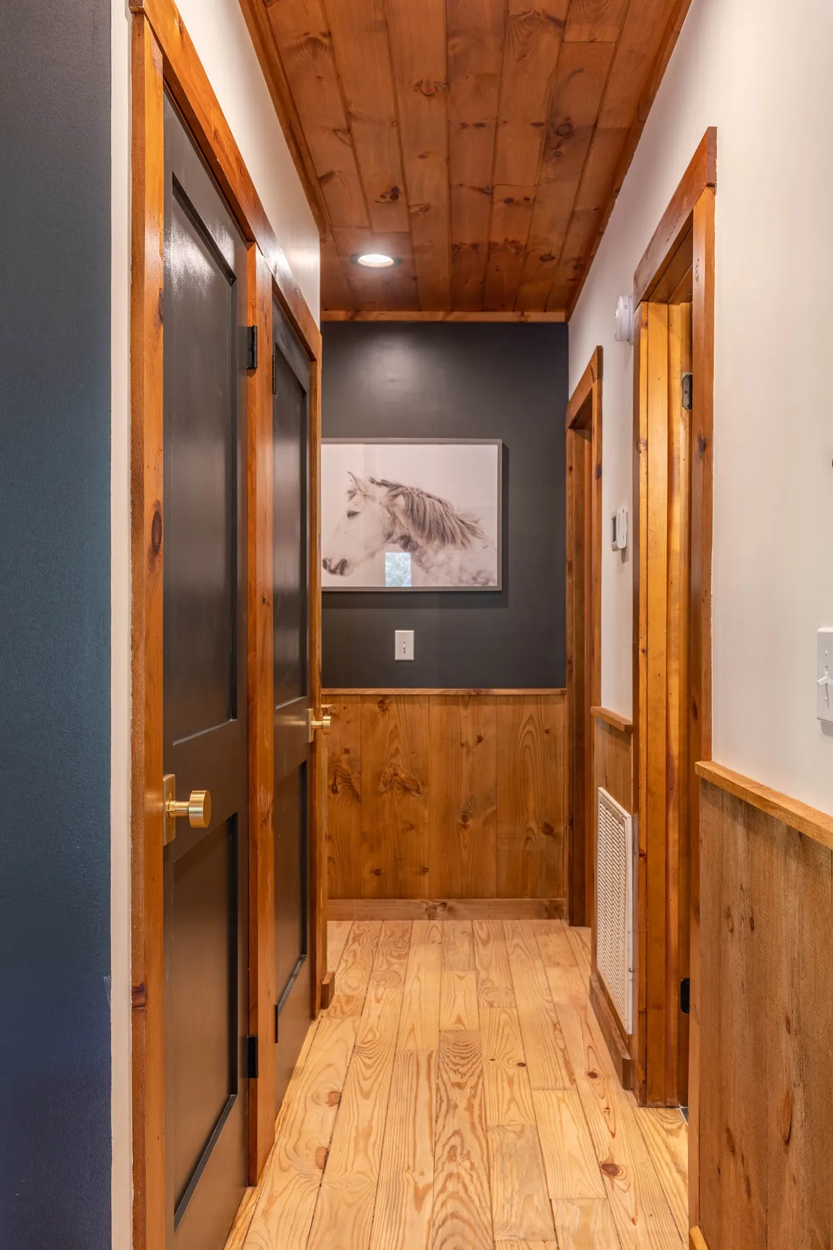 A hallway with prominent wooden doors and ceiling, accented by a striking horse artwork. The inviting passageway exudes warmth and rustic charm, reflecting the cabin's blend of tradition and modern comfort.